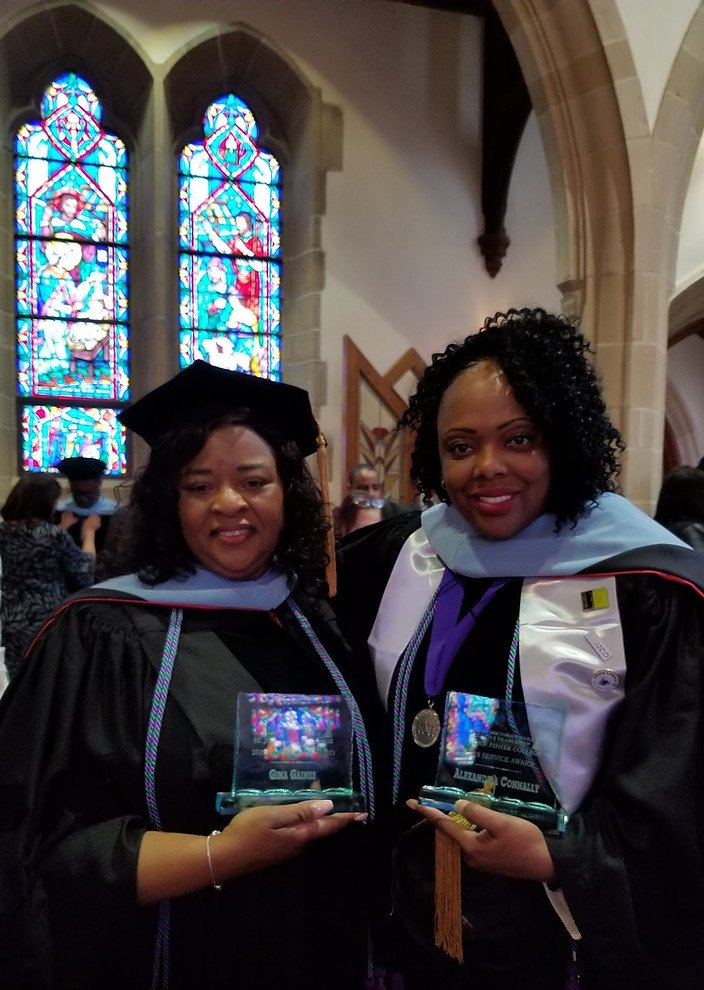 Two Fair Funding leaders in academic regalia holding service awards at a commencement ceremony